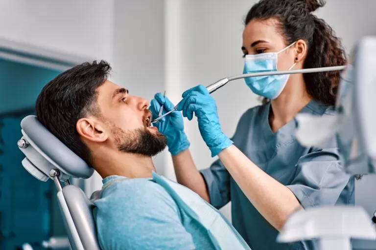 A female dentist in a mask treats a patient's teeth.