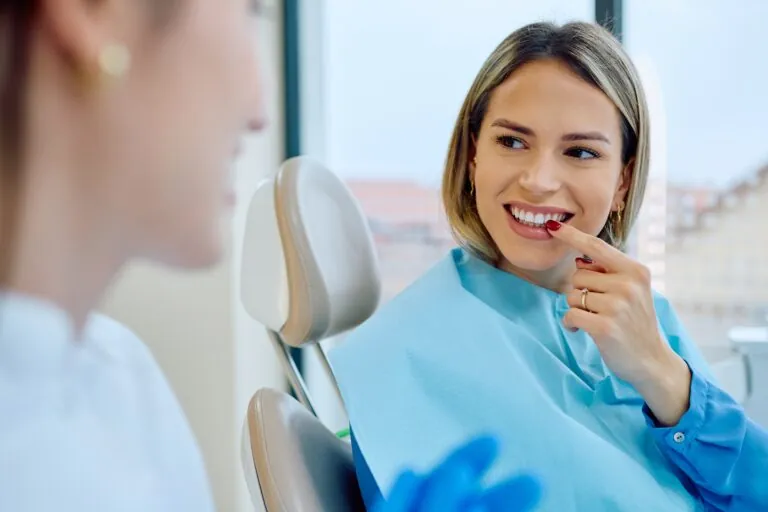 Woman in a dental chair smiling and pointing to her healthy teeth